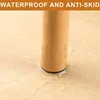 A close-up of a wooden furniture leg with a black anti-slip pad at the bottom, resting on a light-colored wooden floor with some water droplets around it. Produktbild-Vorschau