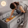 A woman is tending to a baby in a travel crib. Produktbild-Vorschau