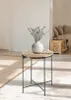 A small round side table with a vase of flowers on top, placed in a room with a rug and a sofa in the background. Produktbild-Vorschau