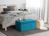 A bedroom scene with a bed, bedding, and a teal storage ottoman. Podgląd zdjęcia produktu