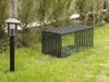 A black metal garden bench and a black lamp post are situated on a grassy lawn with trees in the background. Anteprima dell’immagine prodotto