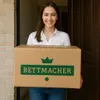 A woman is holding a package in front of a doorway. Produktbild-Vorschau