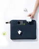 A hand is placing a white charger into the front pocket of a blue laptop bag. A smartphone is already in the pocket, and another charger is visible below. Produktbild-Vorschau