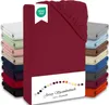 A stack of folded jersey fitted sheets in various colors, with a prominent bordeaux sheet in the foreground. A white label with a green OEKO-TEX logo is attached to the bordeaux sheet. Produktbild-Vorschau
