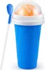 A blue slushy cup with a clear lid, filled with orange slush, and a blue spoon. Podgląd zdjęcia produktu
