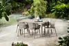 An outdoor patio setting with a table and chairs surrounded by greenery and stairs. Náhled obrázku produktu