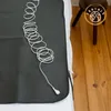 A black grounding mat with a white coiled cord lies on a bed, next to a wooden stool. Produktbild-Vorschau
