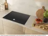 A black induction cooktop is shown on a kitchen counter, with decorative items and food nearby. Anteprima dell’immagine prodotto