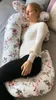 A pregnant woman is sleeping on a bed, using a large C-shaped pillow for support. Náhľad obrázku produktu