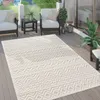 An outdoor rug is placed on a wooden deck, surrounded by outdoor furniture and plants. Voir les images du produit
