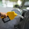 A hand is holding a yellow diesel pump nozzle and inserting it into a car's fuel tank. Produktbild-Vorschau