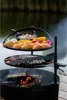 A multi-level grill with food cooking over an open fire, set outdoors near a body of water. Náhled obrázku produktu