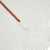 A close-up view of a white umbrella with a wooden handle and white fringe detail. Produktbild-Vorschau