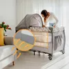 A woman is looking into a baby crib/playpen in a living room setting. Podgląd zdjęcia produktu