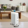 A white oil-filled radiator is placed on a rug in a living room, next to a wooden coffee table and a sofa. Podgląd zdjęcia produktu