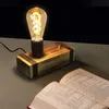 A vintage-style desk lamp with a wooden base sits on a table next to an open book. Produktbild-Vorschau