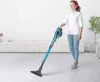 A woman is using a blue stick vacuum cleaner in a modern, well-lit room with white walls and light wooden floors. Produktbild-Vorschau