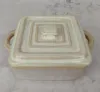 A square ceramic baking dish with a lid and handles, set against a textured gray background. Náhled obrázku produktu
