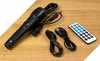 A collection of electronic accessories, including a microphone, cables, and a remote control, laid out on a wooden surface. Produktbild-Vorschau
