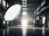 A large UFO high bay LED lamp is suspended in the center of a dimly lit warehouse, with boxes stacked in the background and light streaming from an open doorway. Podgląd zdjęcia produktu