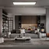 A modern living room and kitchen area with a large gray sofa and a coffee table in the foreground, and kitchen cabinets and appliances in the background. Produktbild-Vorschau