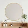A round mirror with a gold frame is displayed on a white wall above a wooden vanity with various cosmetic items. Produktbild-Vorschau