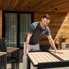 A man is adjusting an extendable outdoor table on a patio. Produktbild-Vorschau