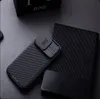 A black iPhone case with a sliding camera cover is placed on a dark textured surface next to a black notebook. Náhled obrázku produktu