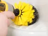 A hand is holding a power drill with a yellow and black brush attachment, cleaning a white surface. Voir les images du produit