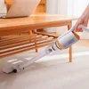 A hand is using a cordless vacuum cleaner to clean a carpet under a wooden table. A laptop is on the table. Produktbild-Vorschau