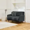 A dark gray corduroy sofa with wooden legs is shown in a well-lit room with a white bookshelf in the background and a patterned rug on the floor. Produktbild-Vorschau