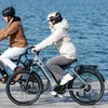 Two people riding electric bikes by the water. Produktbild-Vorschau
