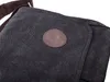A close-up view of a dark canvas messenger bag with a brown leather logo patch. Podgląd zdjęcia produktu