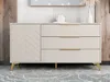 A modern sideboard with a herringbone patterned door and three drawers, on golden legs, displayed in a room with wood-paneled walls and a mirror. Náhľad obrázku produktu