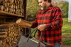 A man is holding a piece of firewood and a felt bag filled with firewood, standing next to a woodpile. Náhled obrázku produktu