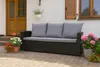 A dark rattan sofa with gray cushions sits on a brick patio in front of a white house. Potted plants with pink and red flowers are placed around the sofa. Anteprima dell’immagine prodotto
