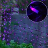Purple LED string lights are draped over a fence with green foliage in the foreground. Produktbild-Vorschau