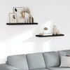 Two black floating shelves mounted on a white wall, decorated with various vases, books, and framed art. A portion of a gray sofa is visible in the foreground. Náhled obrázku produktu