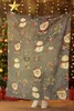 A person is standing behind a Christmas-themed blanket with Santa Claus, snowmen, and gingerbread men patterns. Náhled obrázku produktu