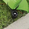 A close-up view of a green string trimmer with a black wheel, resting on grass next to a concrete edge. Produktbild-Vorschau