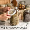 A close-up shot of hands holding a glass jar lid, with several glass jars filled with food items in the background. Podgląd zdjęcia produktu