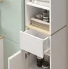 A close-up view of a white cabinet with a drawer partially open, revealing storage shelves and bottles inside. A light green wall is visible in the background. Voir les images du produit