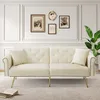 A cream-colored sofa with gold legs is shown in a well-lit room with decorative wall art and a plant.