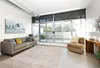 A modern living room with a sofa, armchair, rug, and large sliding glass doors leading to a patio. Produktbild-Vorschau