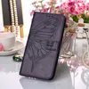 A purple flip leather phone case with a butterfly embossed design is displayed on a reflective surface, with a cup and saucer and flowers in the background. Produktbild-Vorschau