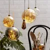 Decorative glass orbs filled with fairy lights, hanging in a room with a brick wall background and some plants and art supplies in the foreground. Produktbild-Vorschau
