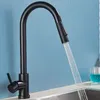 A black kitchen faucet with water running into a sink, with a glass of blue liquid in the background. Produktbild-Vorschau
