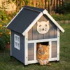 A cat is resting inside a wooden cat house in a garden. Produktbild-Vorschau
