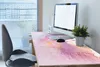 A desk with a computer, keyboard, mouse, and a potted plant, featuring a large desk mat with a watercolor-like design. Produktbild-Vorschau