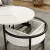 A round coffee table with a marble-like finish is shown with its top lifted, revealing storage space inside. The table is placed on a gray rug in a living room setting. Anteprima dell’immagine prodotto